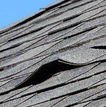 Damaged asphalt roof shingles, torn and curled upward.