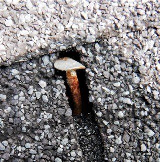 Rusty nail sticking out of asphalt.