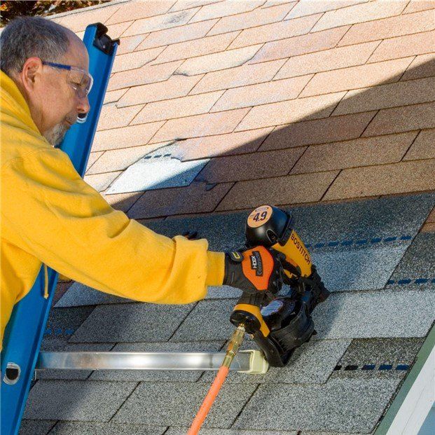 Man using a nail gun to repair a roof. Yellow jacket, safety glasses, holding a pneumatic tool with orange air hose.