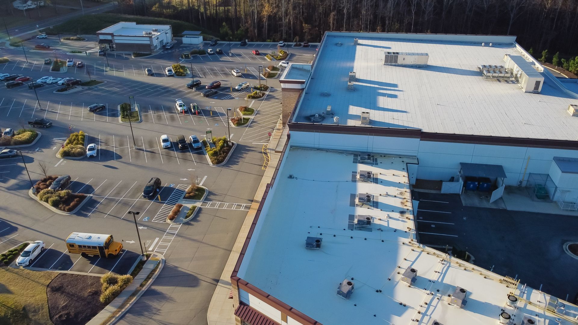 Aerial view of a commercial building with a large parking lot and surrounding trees.