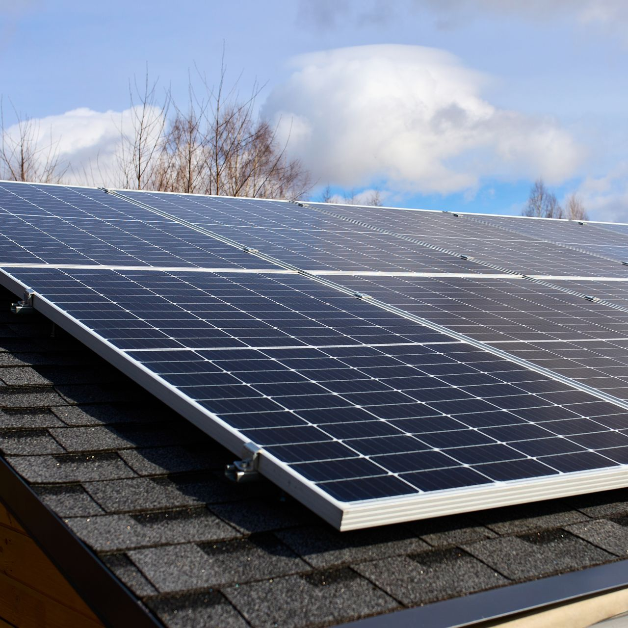 Solar panels on a shingled roof under a partly cloudy sky.