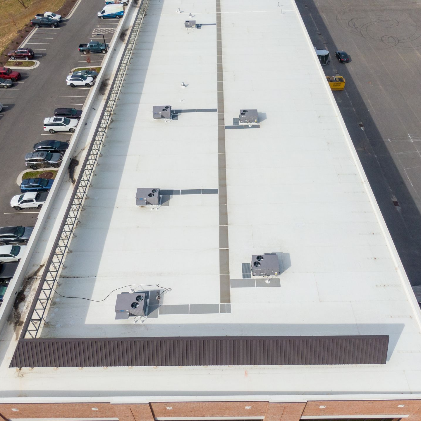 Aerial view of a white commercial roof with HVAC units. Cars parked below.