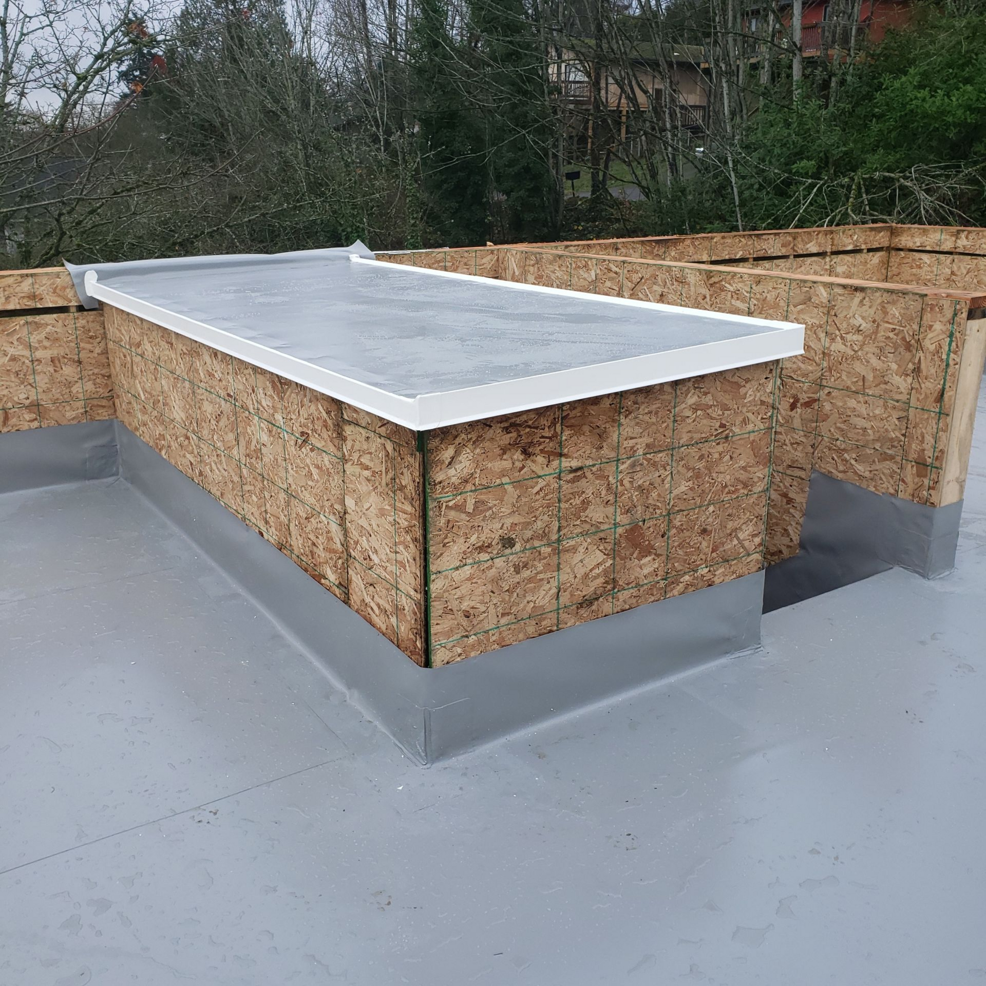 Flat roof under construction with OSB walls and gray roofing membrane.