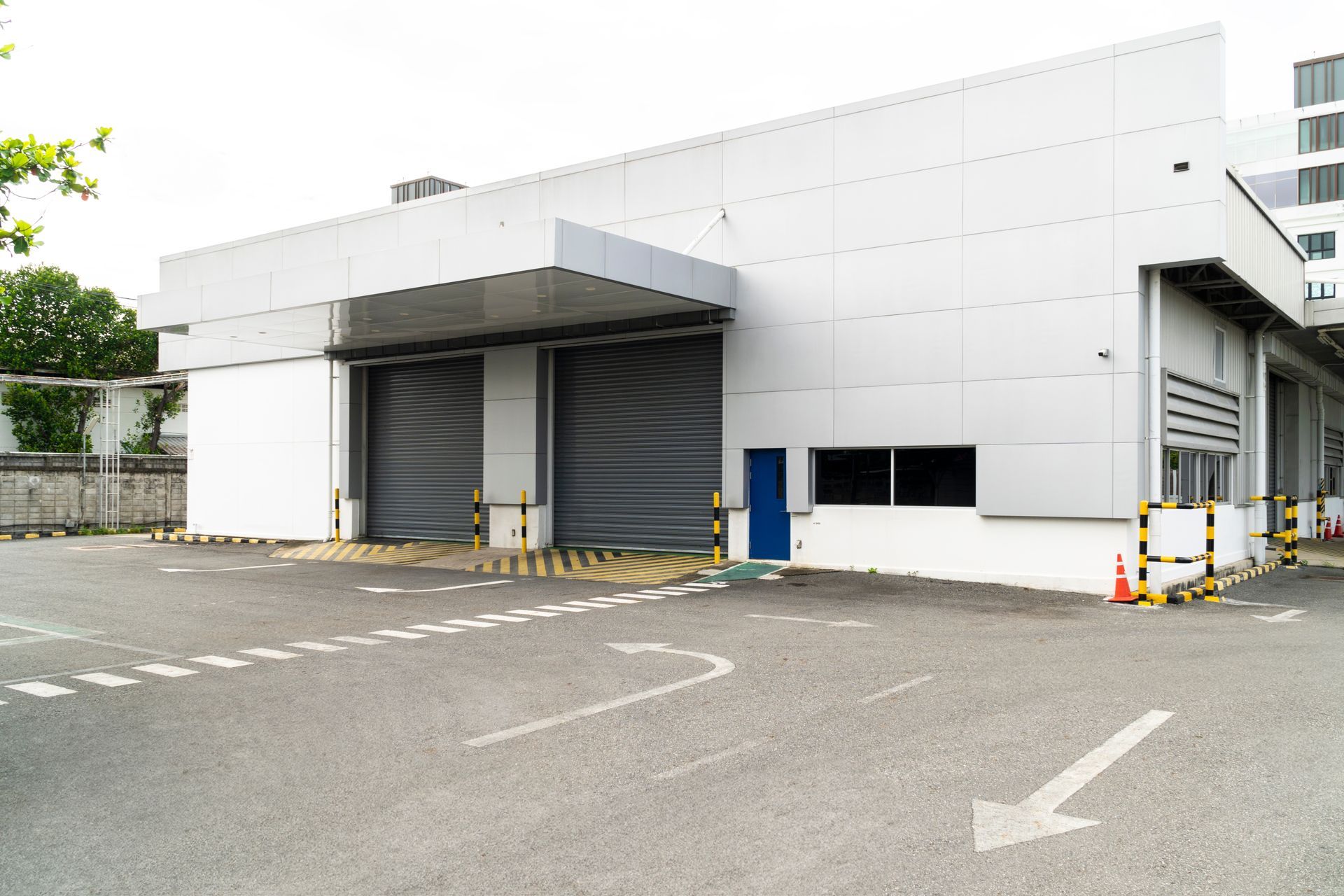 Exterior of a light industrial building with two roller doors, asphalt parking, and directional arrows.