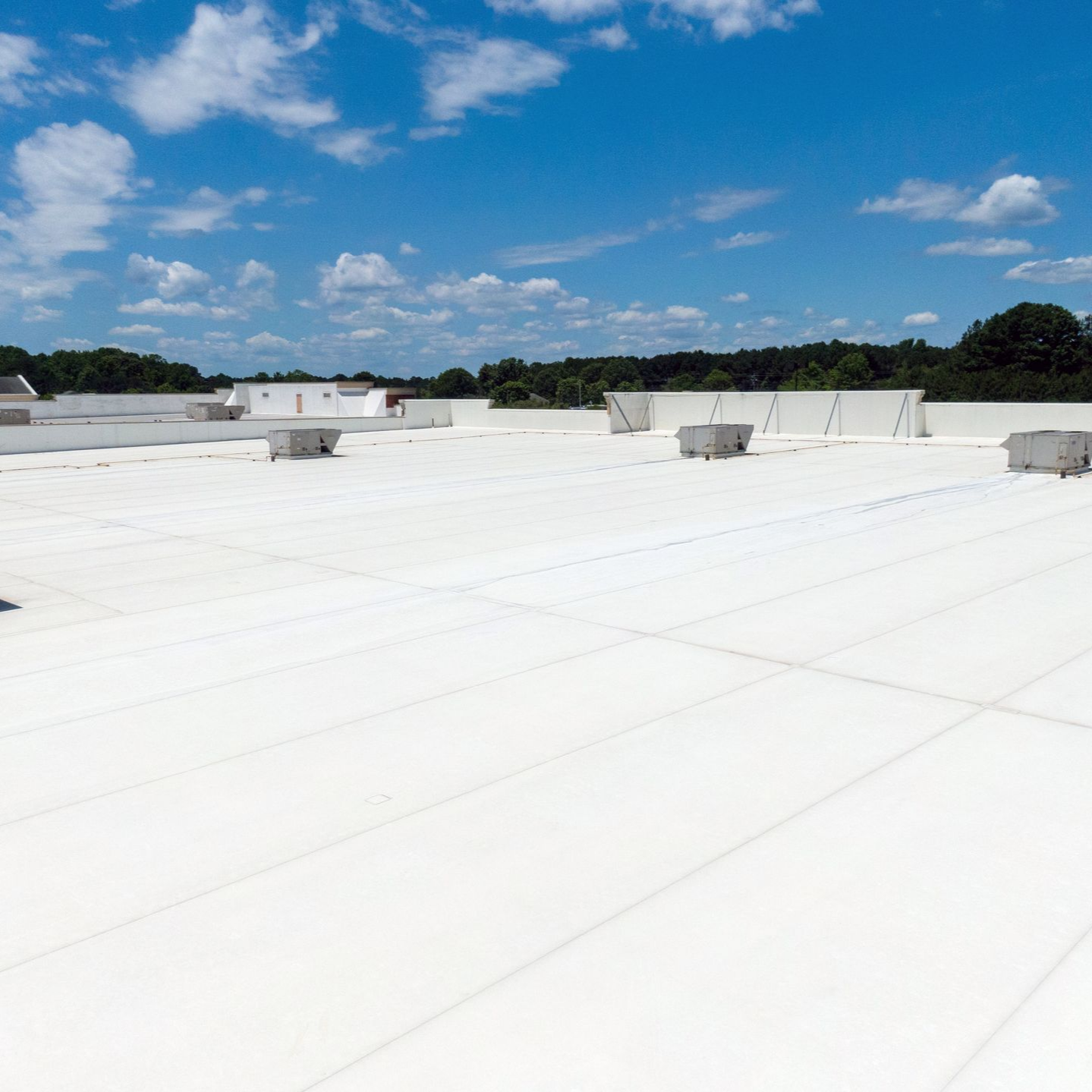 White commercial flat roof with vents under a blue sky.