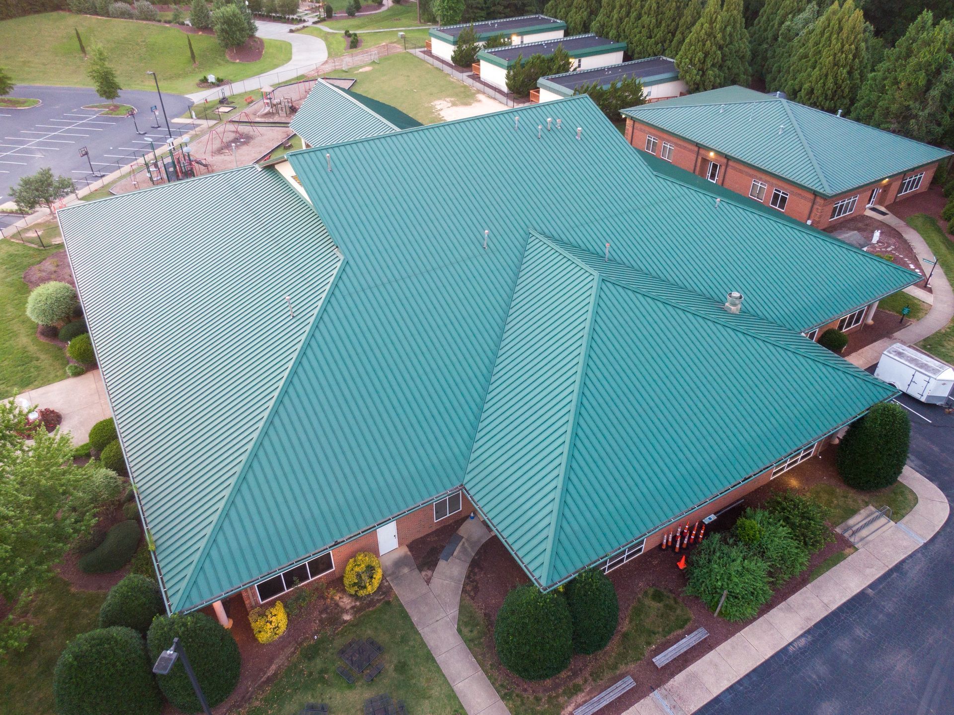 Aerial view of a teal corrugated metal roof on a building with a playground and trees in the background.