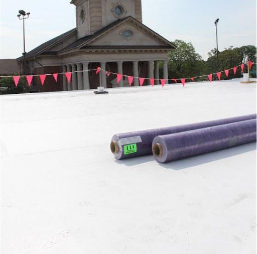 White roof with rolls of material, pink flags, and a building with columns in the background.