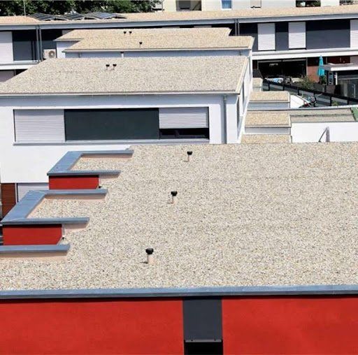 Flat roofs covered with small stones on a building with white walls, red accents, and dark shutters.