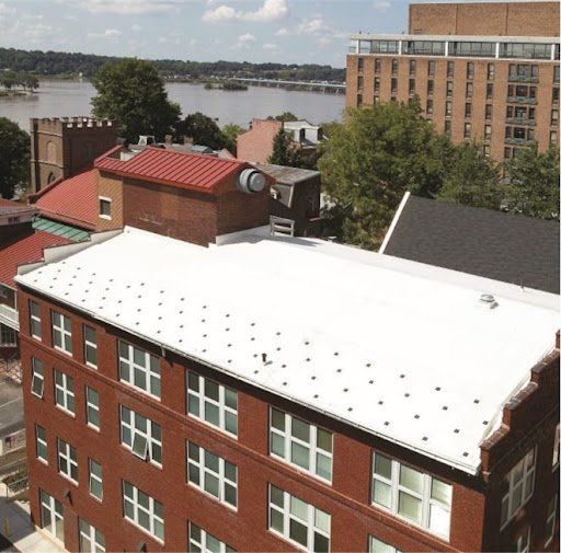 An aerial view of a red brick building with a white roof and river in the background.