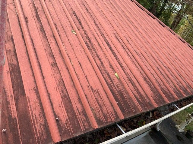 Weathered red corrugated metal roof with peeling paint, showing signs of oxidation and debris in the gutter.