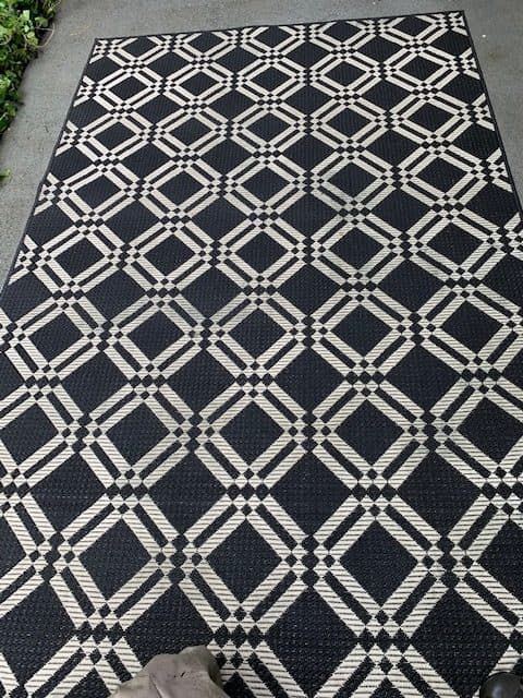 A black and white area rug with a repeating geometric diamond and lattice pattern, displayed on a patio or walkway.