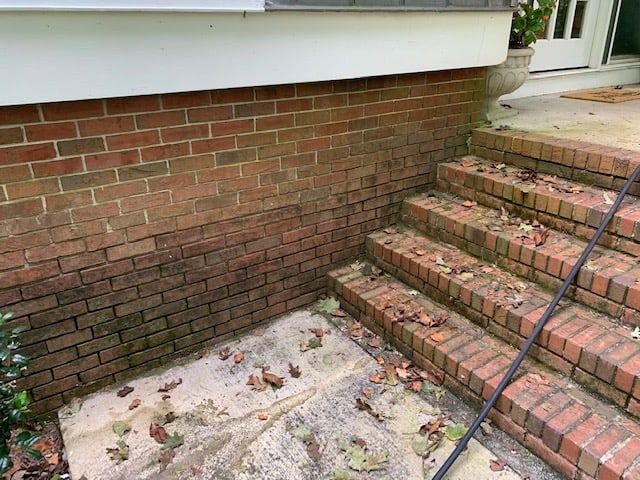 Red brick foundation wall and matching steps with scattered fallen leaves, next to a concrete walkway.