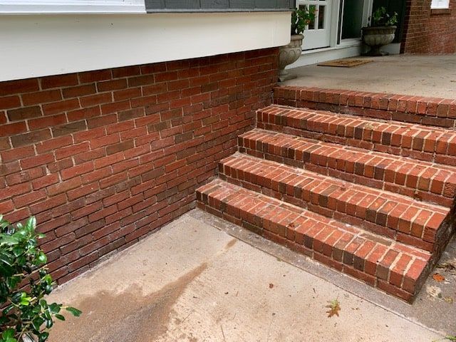 Red brick steps leading to a concrete porch with a white trim along the brick wall on the left.