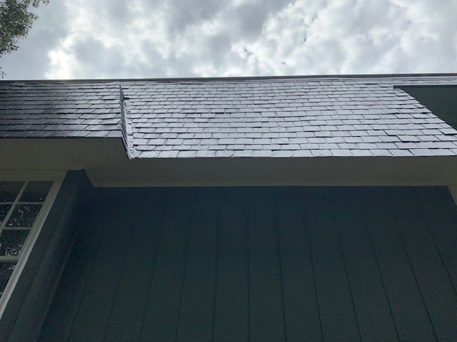 Low-angle view of a grey shingled roof with a slight structural offset against a cloudy sky.