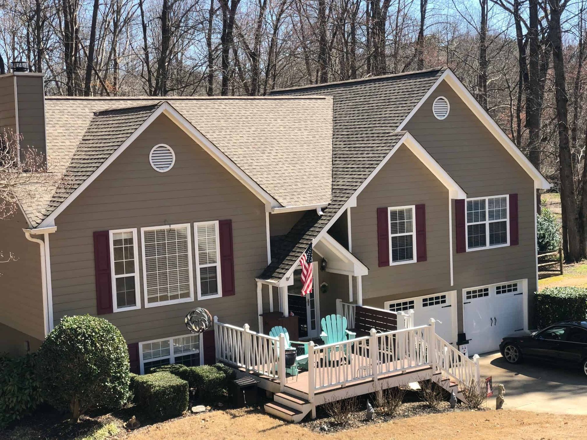 A two-story tan house with a dark roof, maroon shutters, a front deck with teal chairs, and a two-car garage.