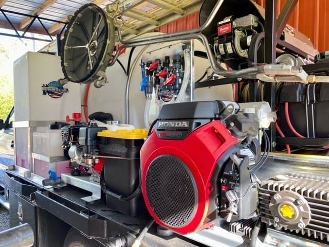 A red Honda engine mounted on a flatbed truck setup with industrial tanks, hoses, and cleaning equipment.