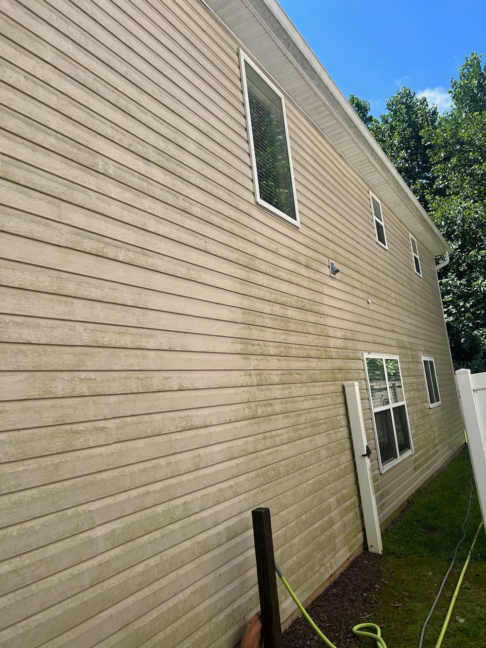 Side view of a two-story beige house exterior showing vinyl siding with visible streaks of dirt and algae.