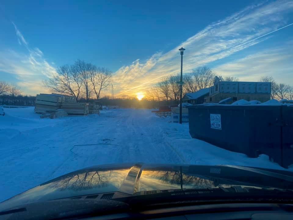 A car is driving down a snowy road at sunset.