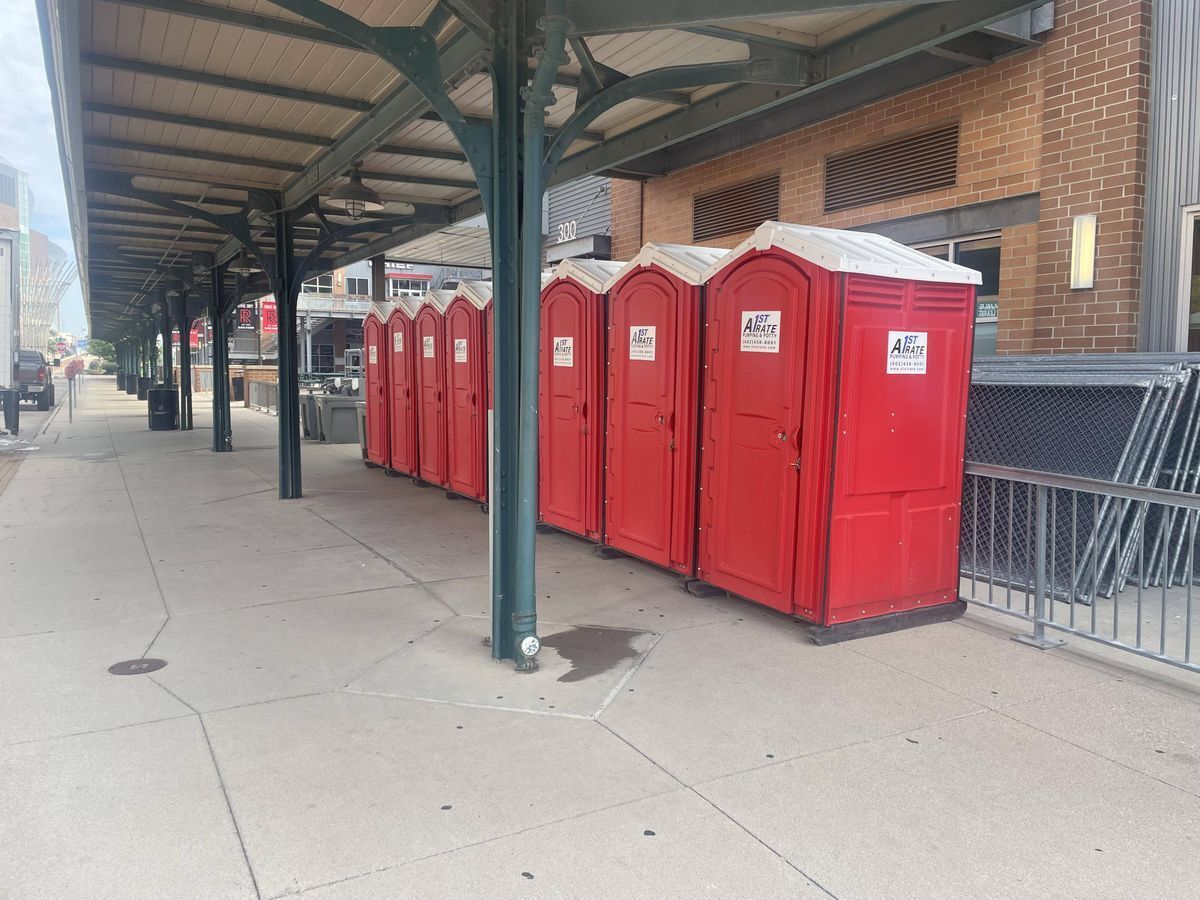 A row of red portable toilets are lined up on a sidewalk.