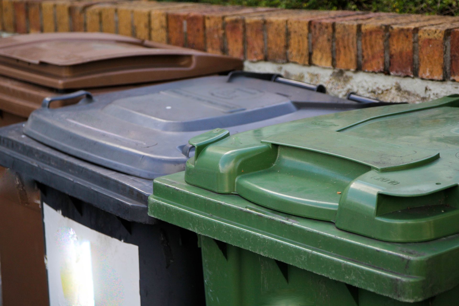 A group of trash cans are sitting next to each other in front of a brick wall.