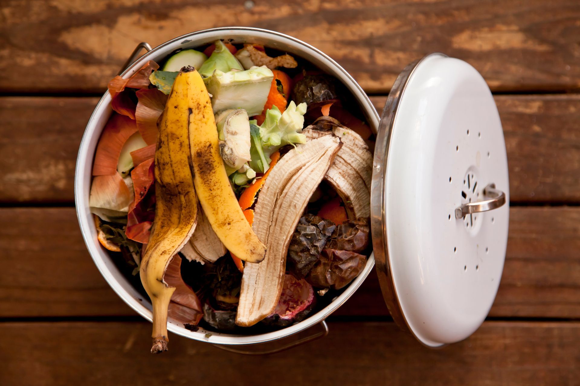 A white trash can filled with food scraps on a wooden table.