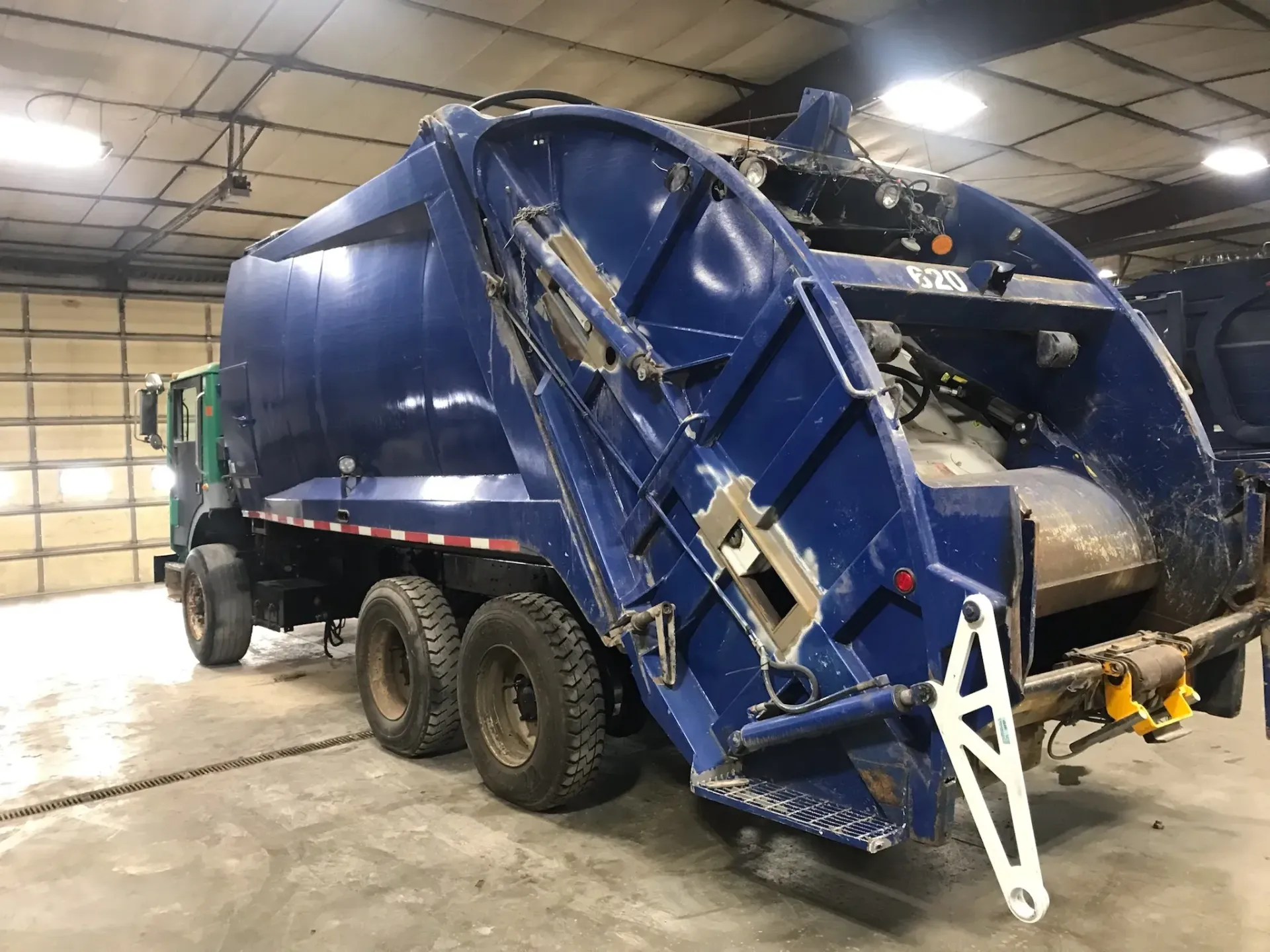 A blue garbage truck is parked in a garage.