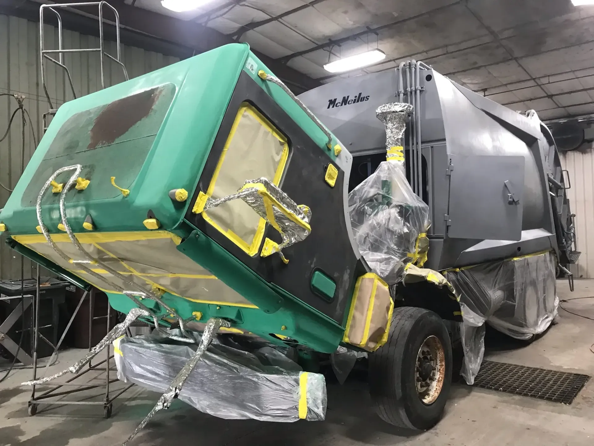 A garbage truck is being painted in a garage.