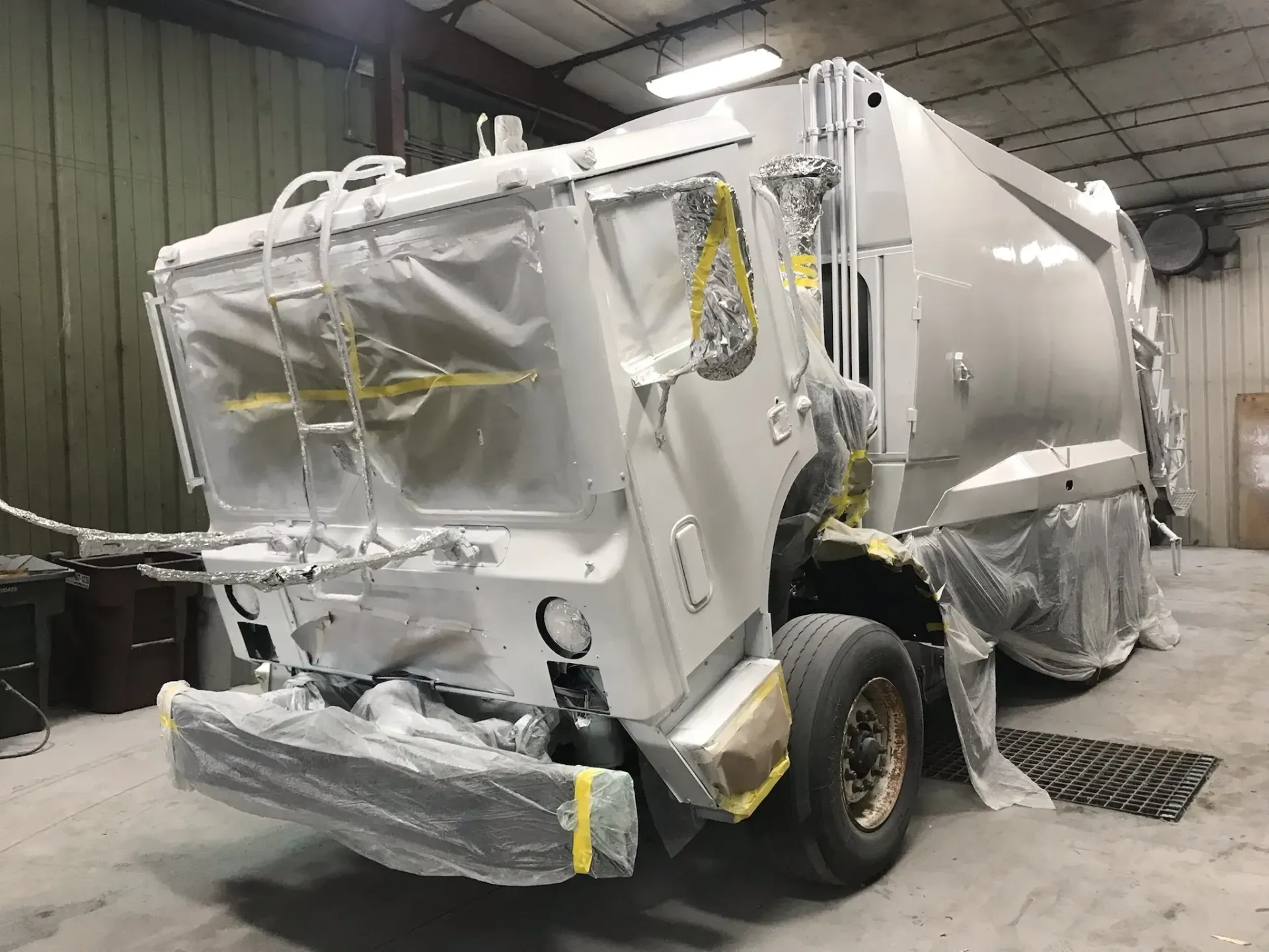 A white garbage truck is being painted in a garage.