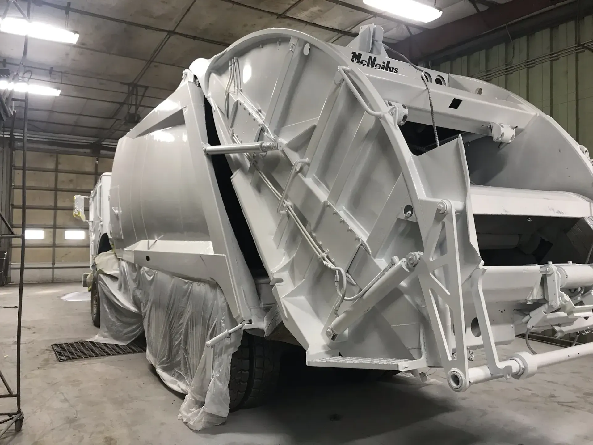A white garbage truck is being painted in a garage.