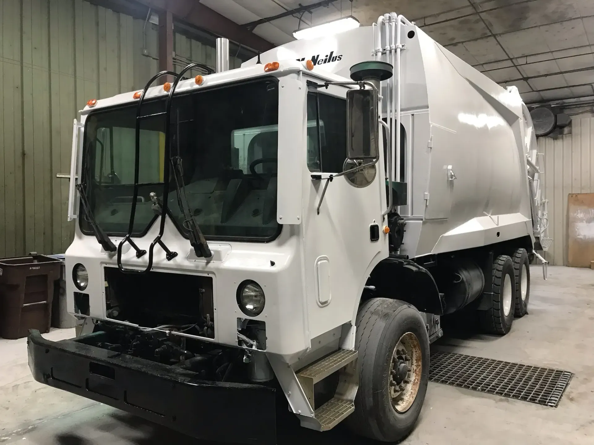 A white garbage truck is parked in a garage.