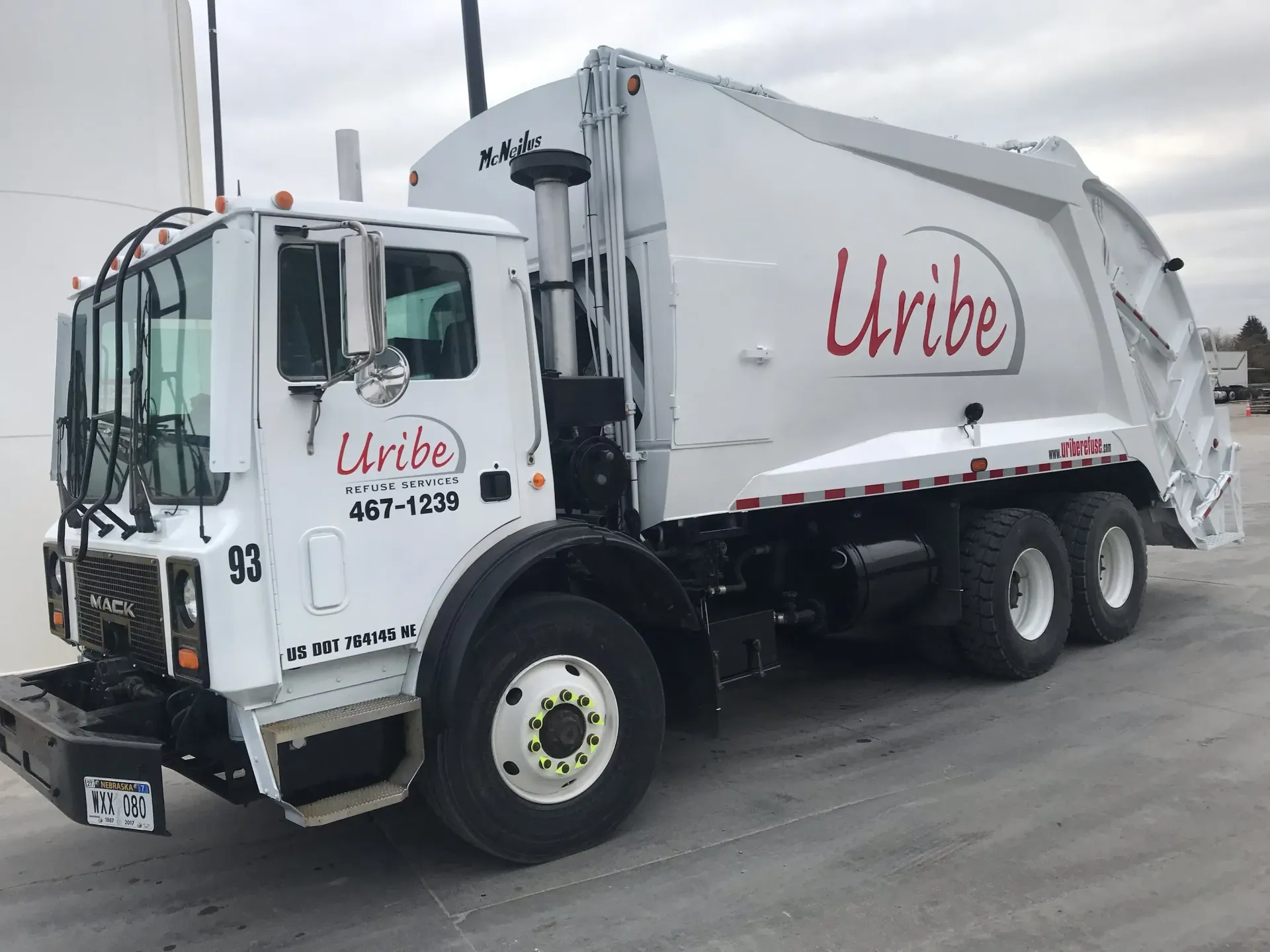 A white garbage truck is parked in a parking lot.