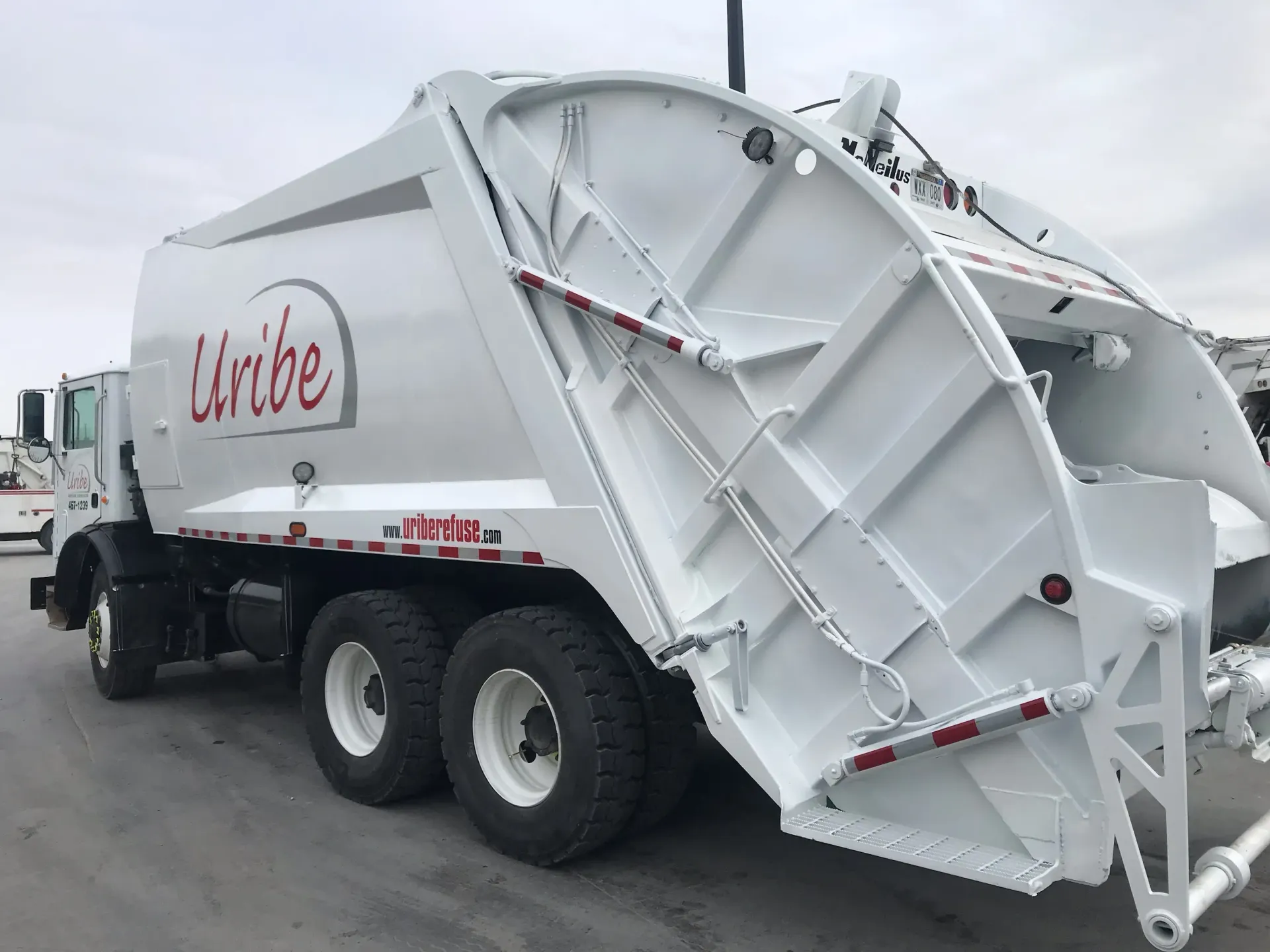 A white garbage truck is parked in a parking lot.