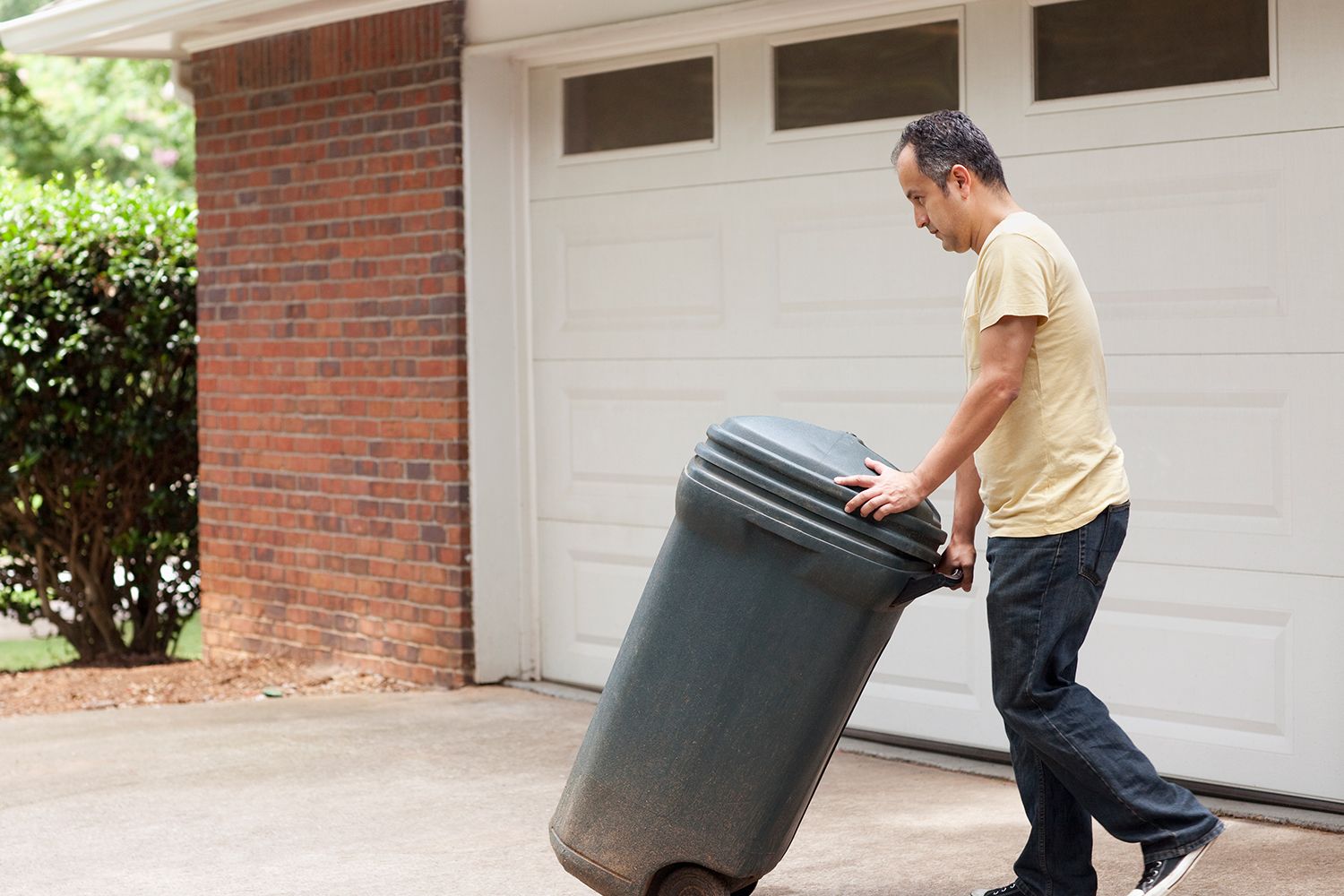 Man rolling a trash can.
