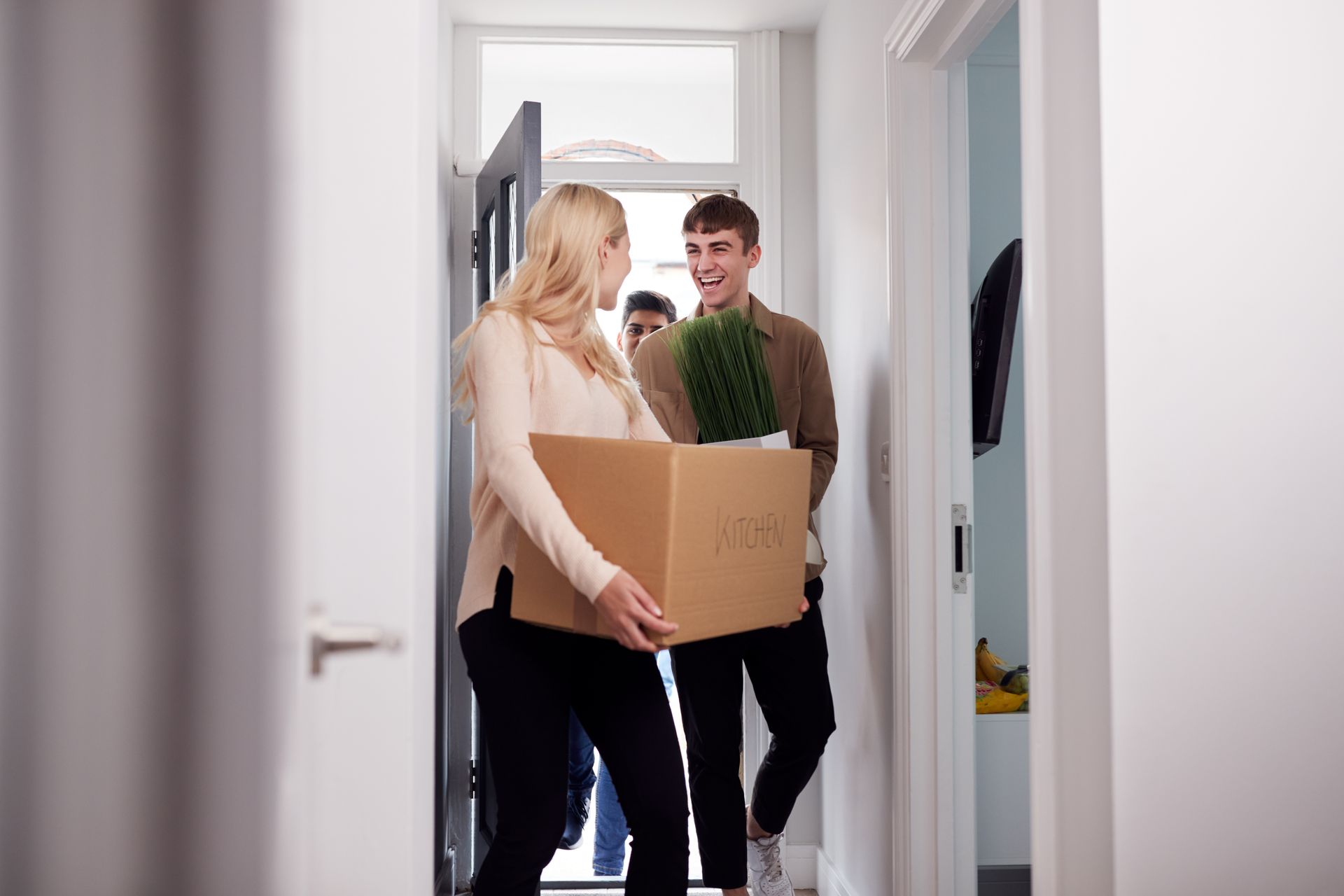 People carrying boxes and plants into a home's entryway.