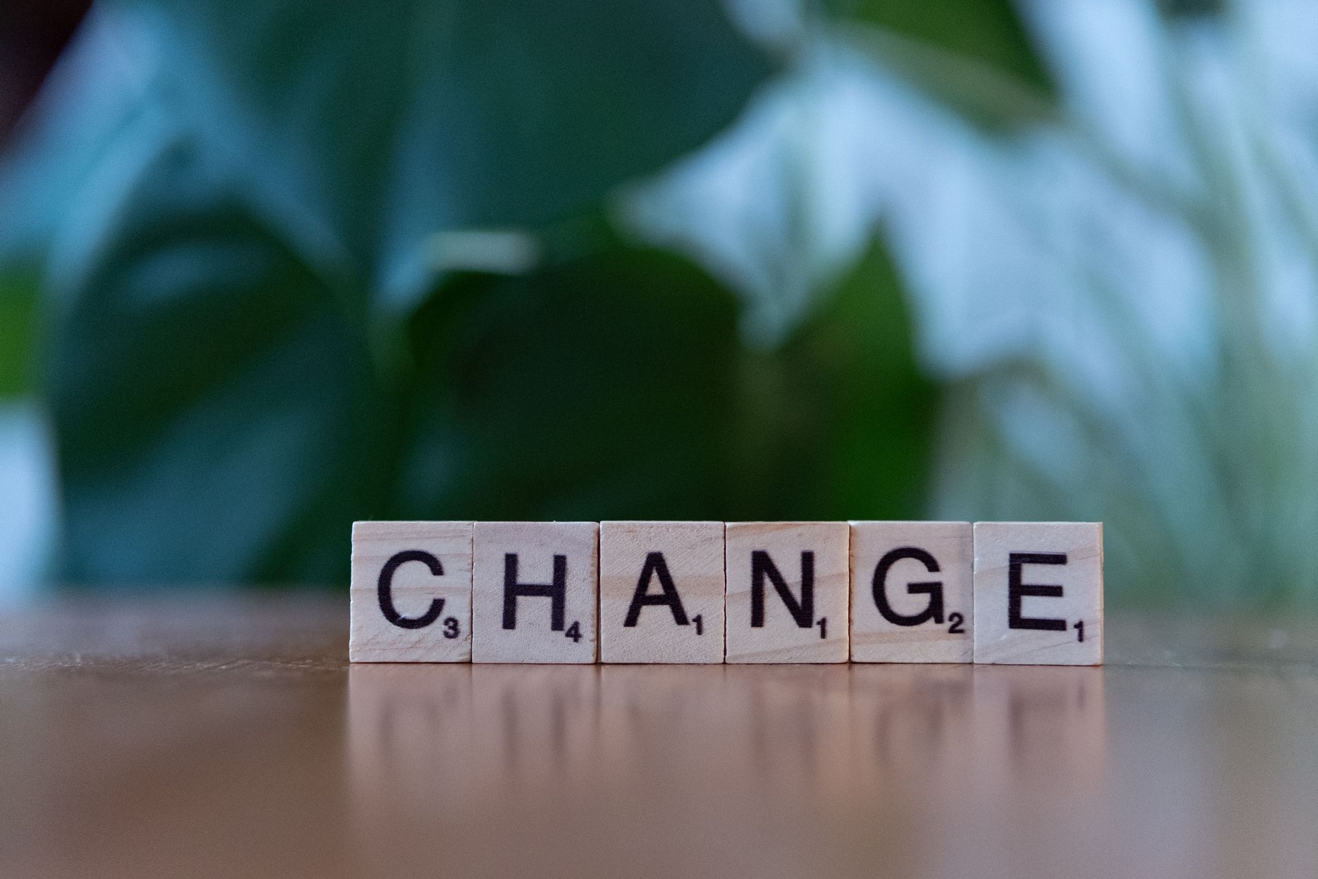 Letter tiles spelling “CHANGE” on a table with a blurred green background.