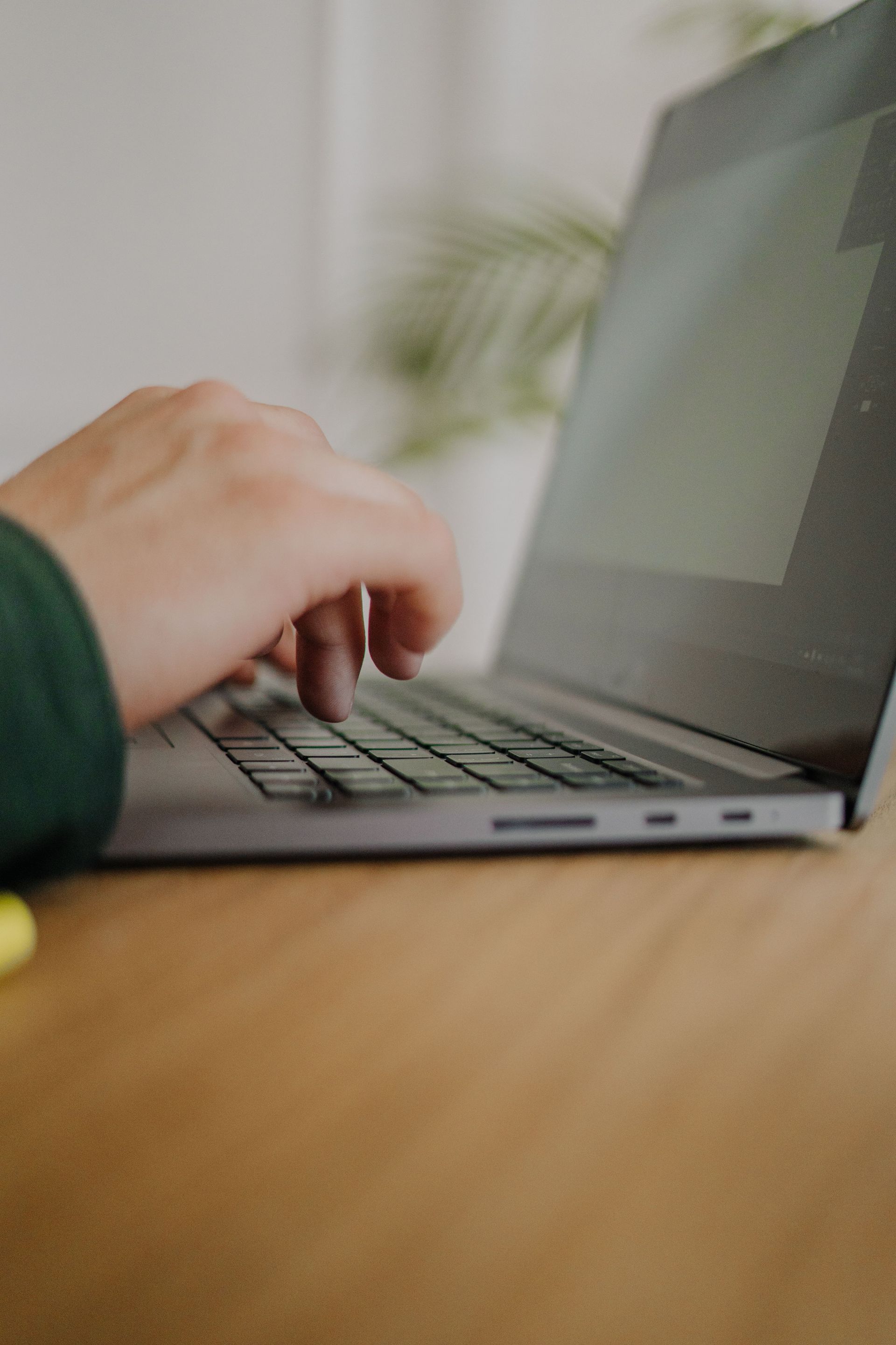 Hands typing on a laptop keyboard at a wooden desk.