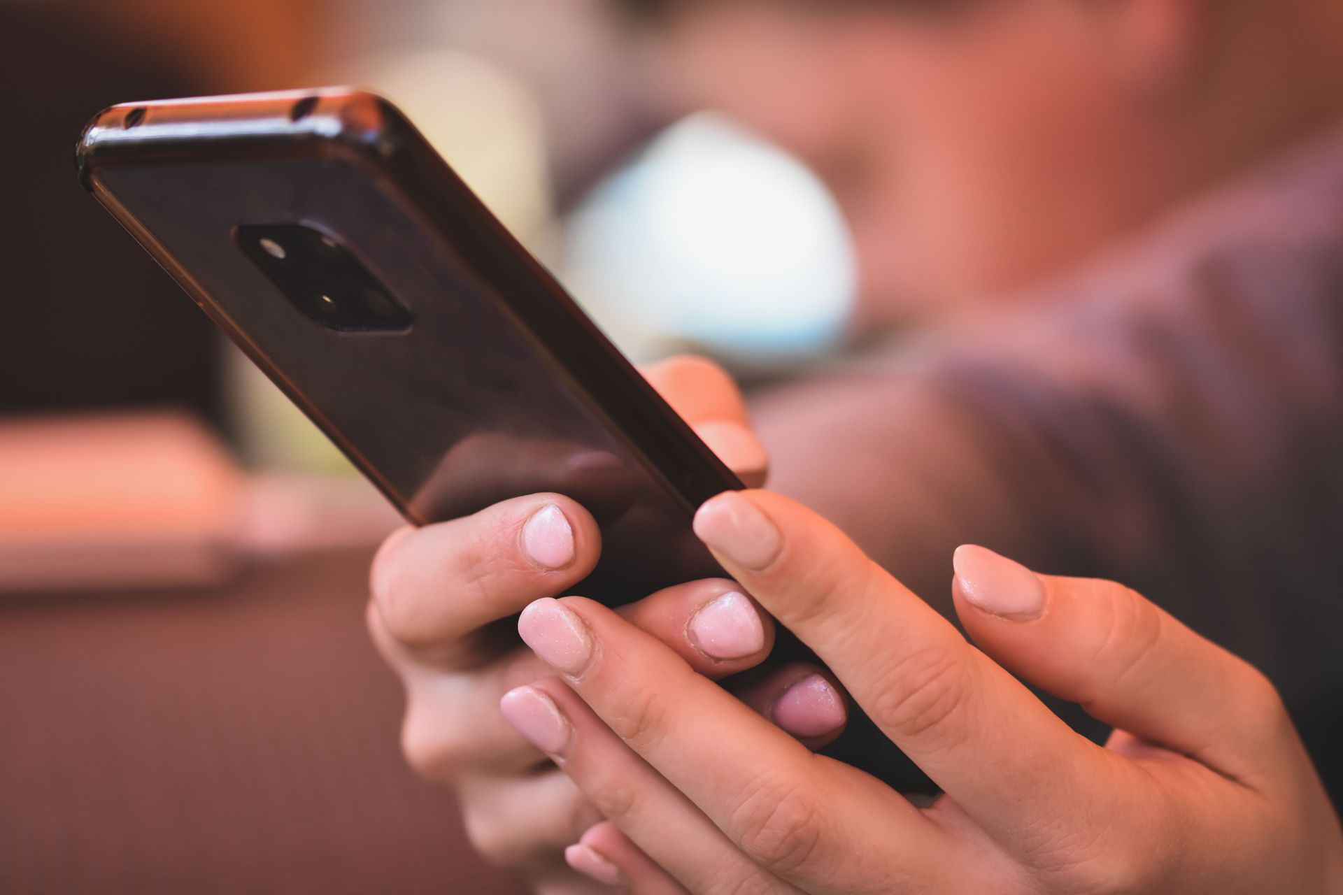 Hands holding a black smartphone in a blurred indoor setting