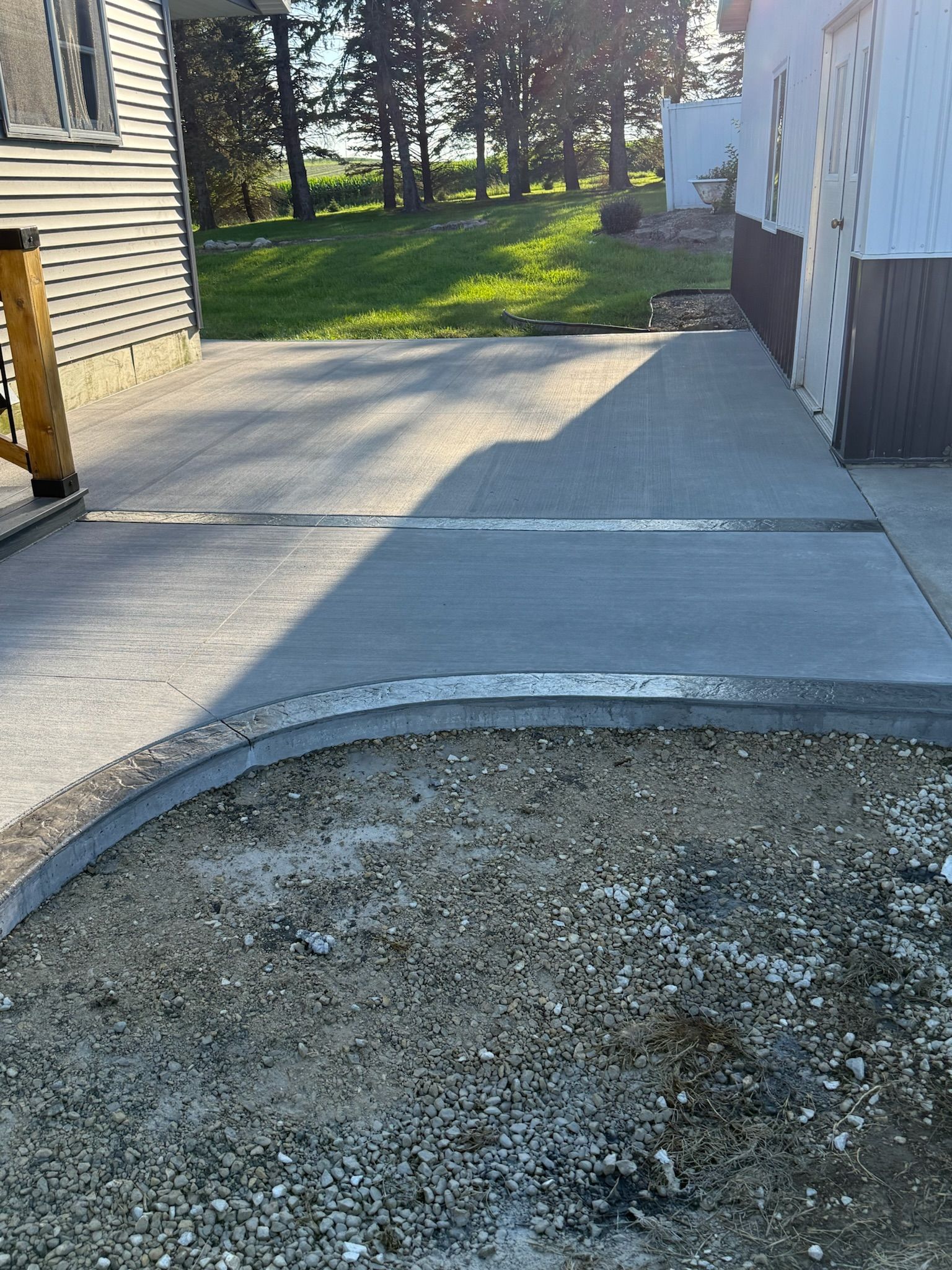 A freshly poured concrete patio bordered by a curved retaining wall, situated next to the side of a house.