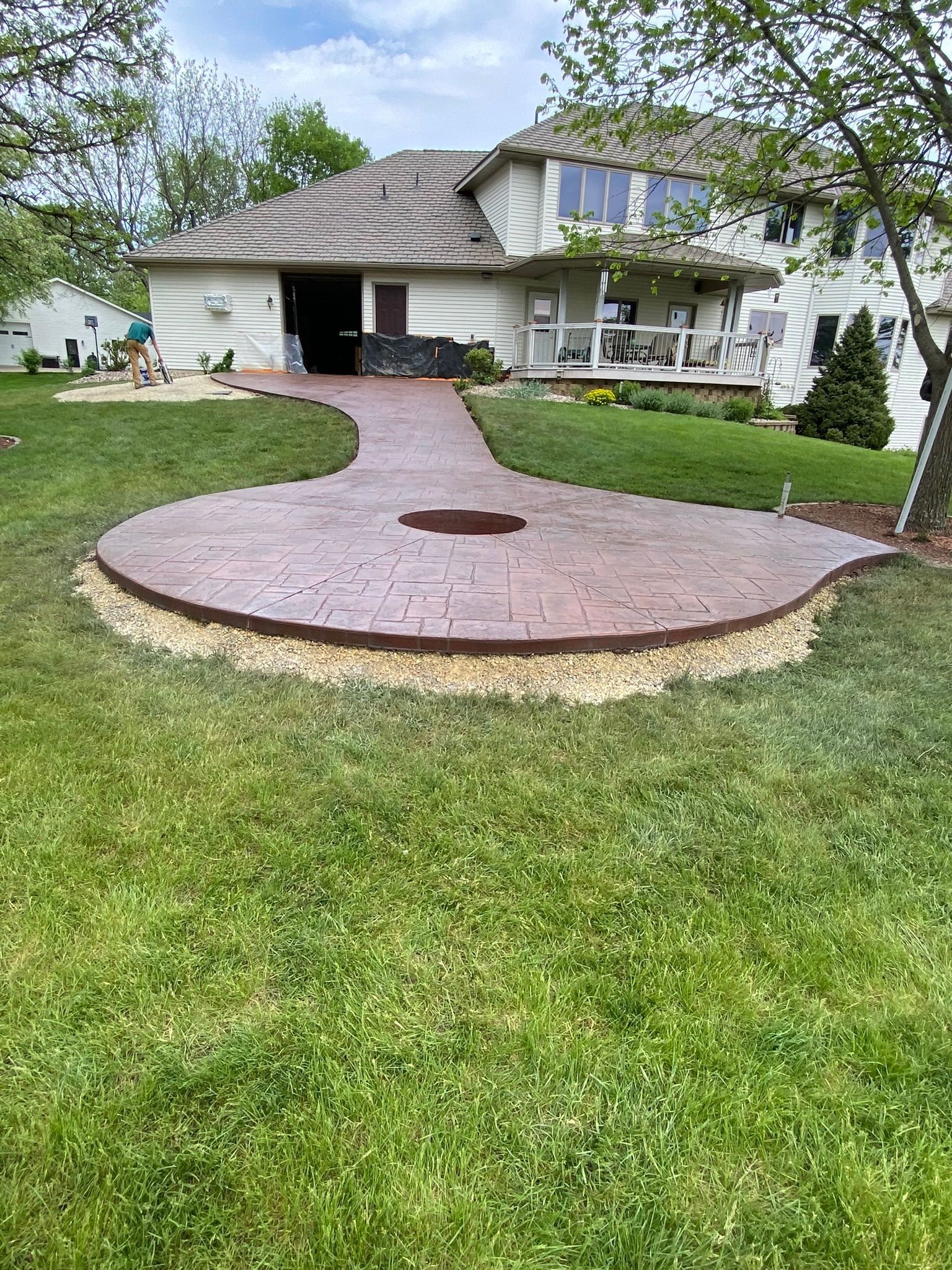 A new brown stamped concrete patio and walkway extend from a residential house into a grassy backyard.