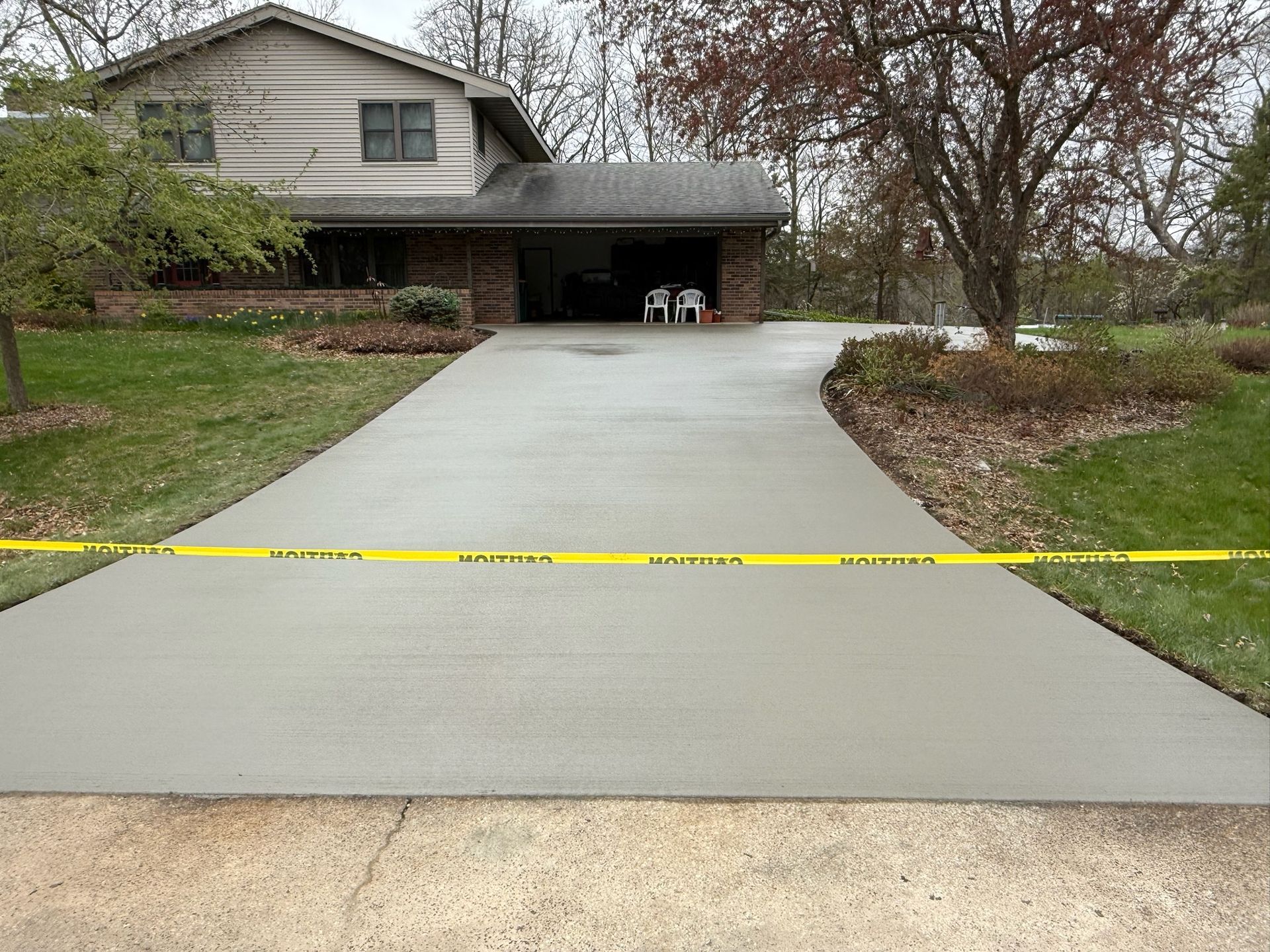 A freshly poured concrete driveway leads to a suburban house, blocked by yellow caution tape.