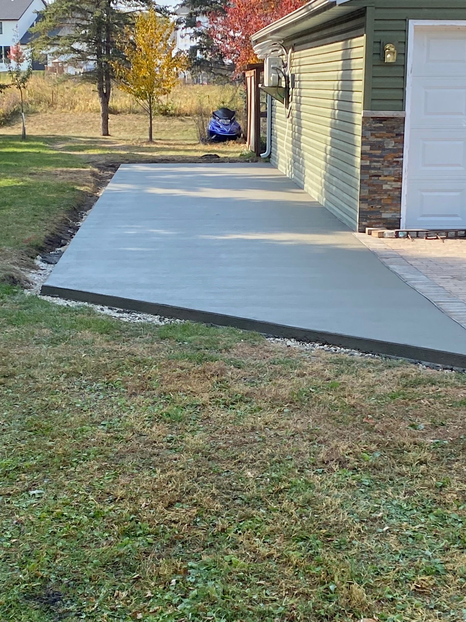 A newly poured, rectangular concrete patio extending from the side of a garage next to a grassy lawn.