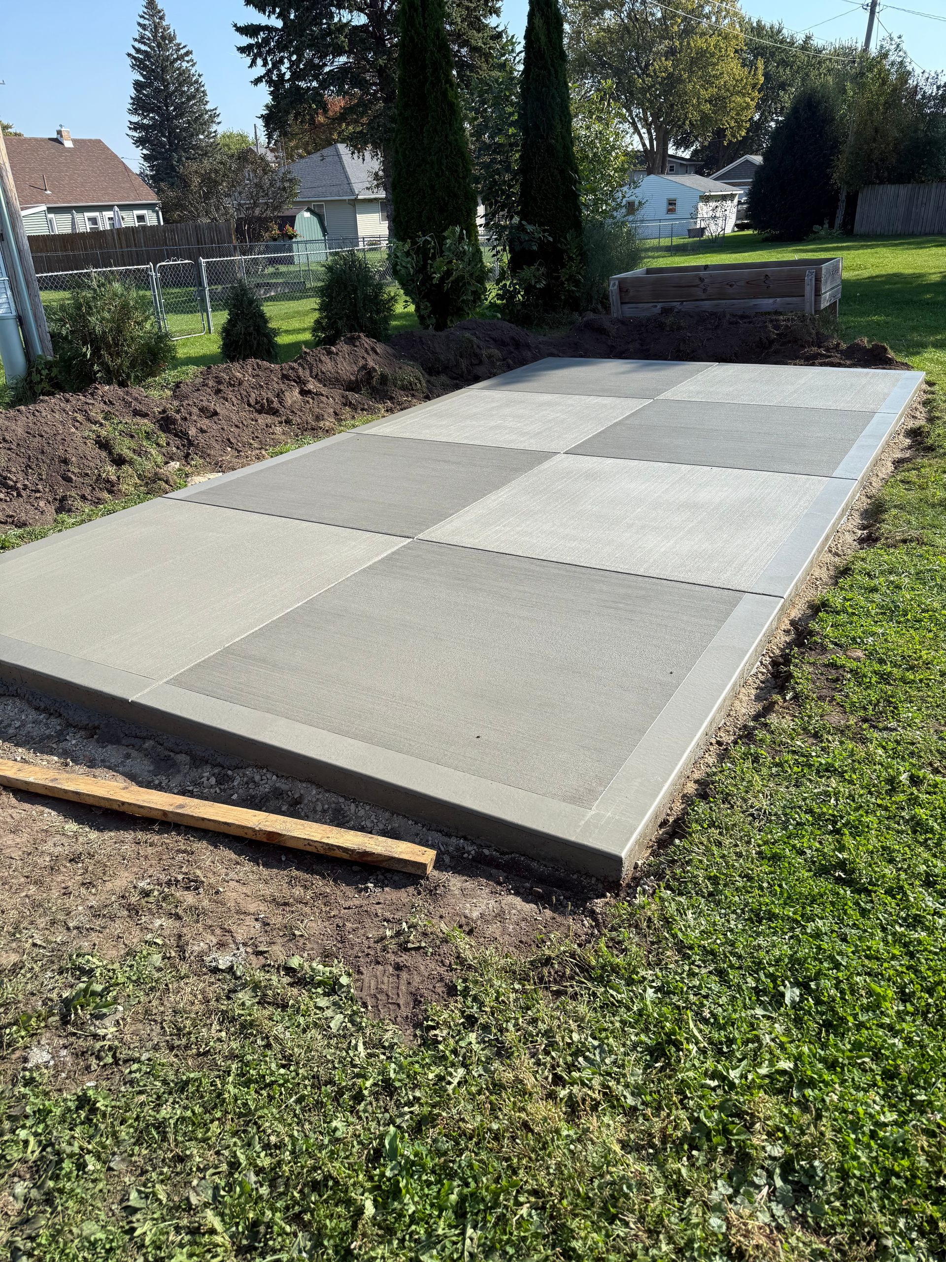 A rectangular patio foundation built from alternating gray pavers and interlocking foam tiles on a grassy lawn.