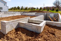 Concrete foundation walls for a new house under construction on a dirt lot with a nearby home in the background.