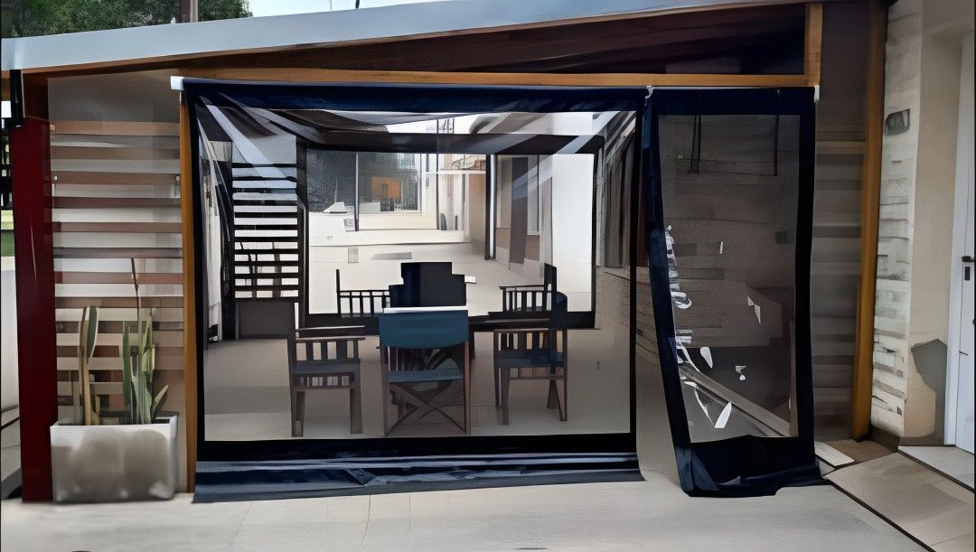 Comedor exterior cubierto con cerramiento transparente de marco negro y mesa y sillas en el interior.