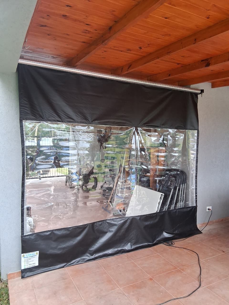 Cerramiento de patio negro con ventanas de vinilo transparente bajo un techo de madera en un porche.
