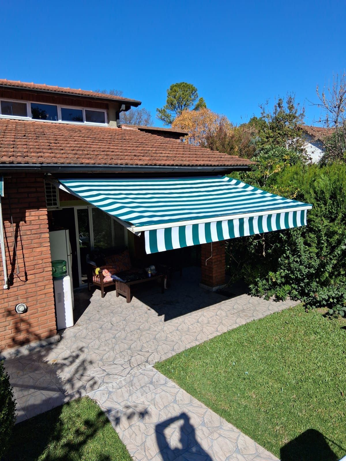 Patio trasero con toldo a rayas verdes y blancas junto a una casa de ladrillo en un día soleado.