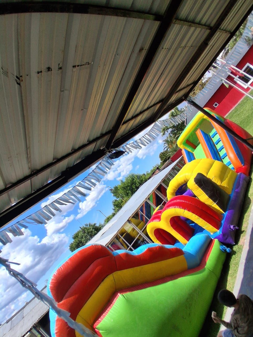 Circuito de obstáculos inflable y colorido bajo un techo de metal en un campo de hierba, vista inclinada.