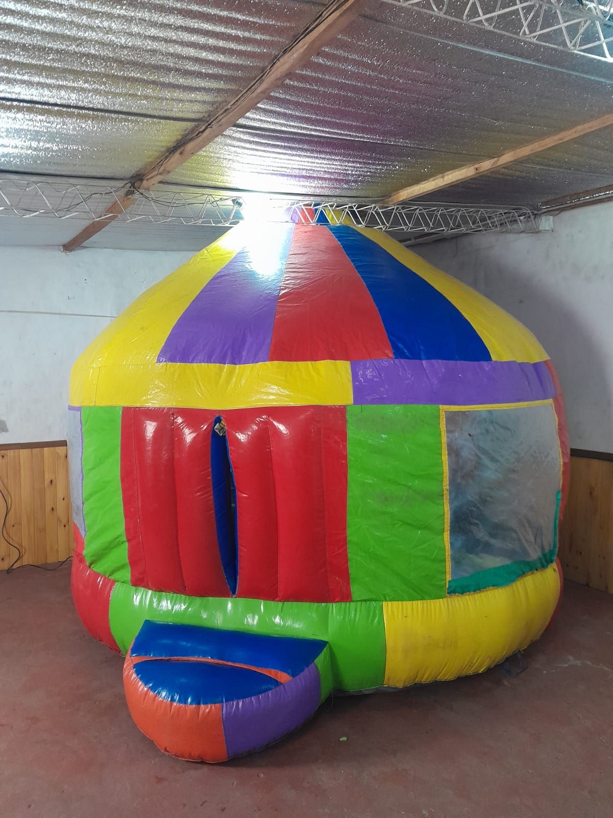 Casita de juegos inflable de colores con paneles interiores rojos, amarillos, verdes, azules y morados.