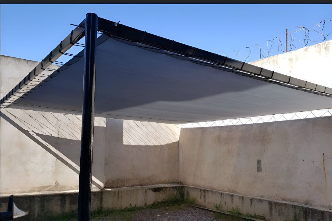 Toldo triangular de vela de sombra en un pequeño patio de hormigón bajo un cielo azul despejado.
