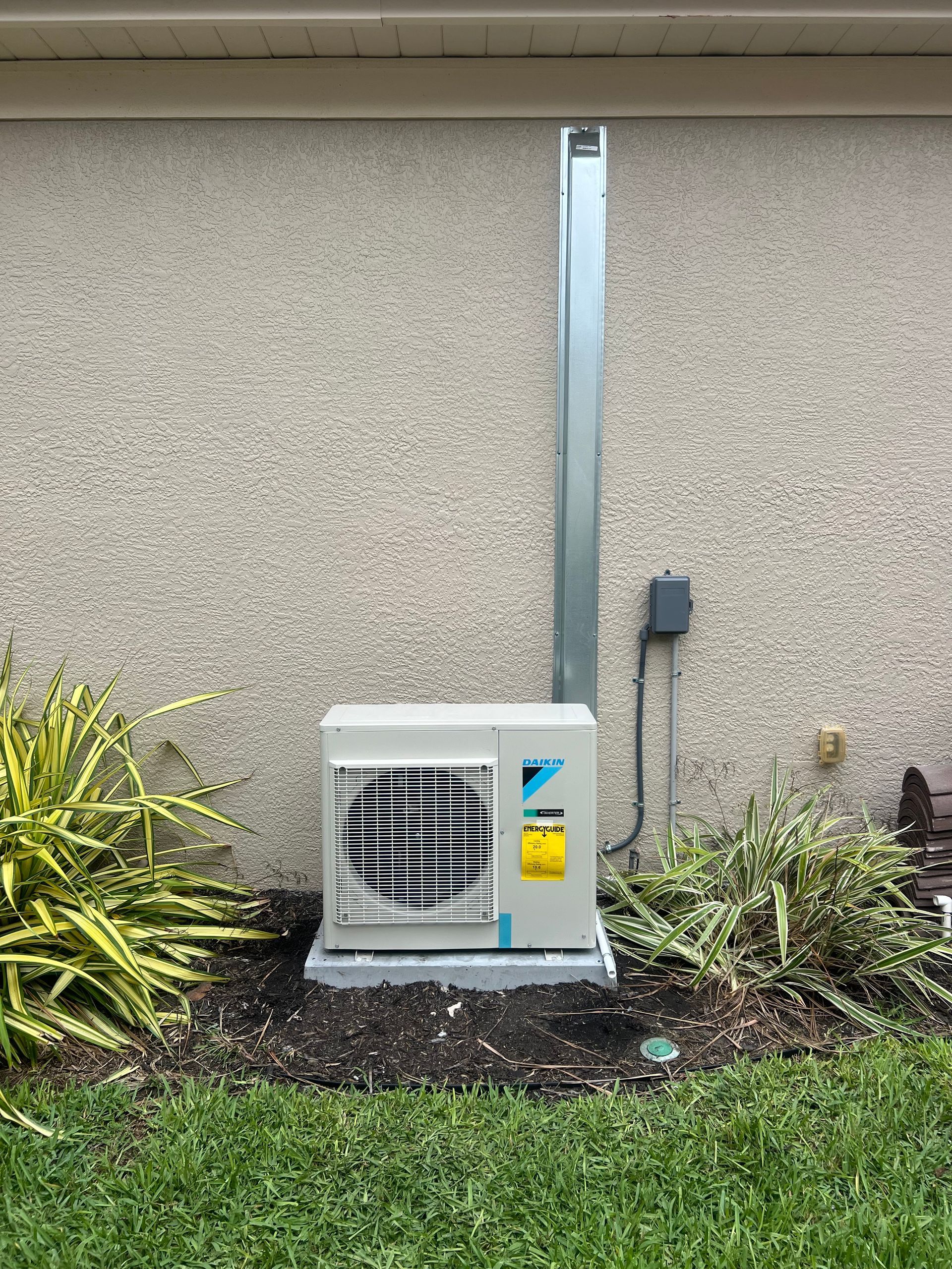 Air conditioning unit mounted on a concrete pad outside a stucco wall with a conduit and power box.